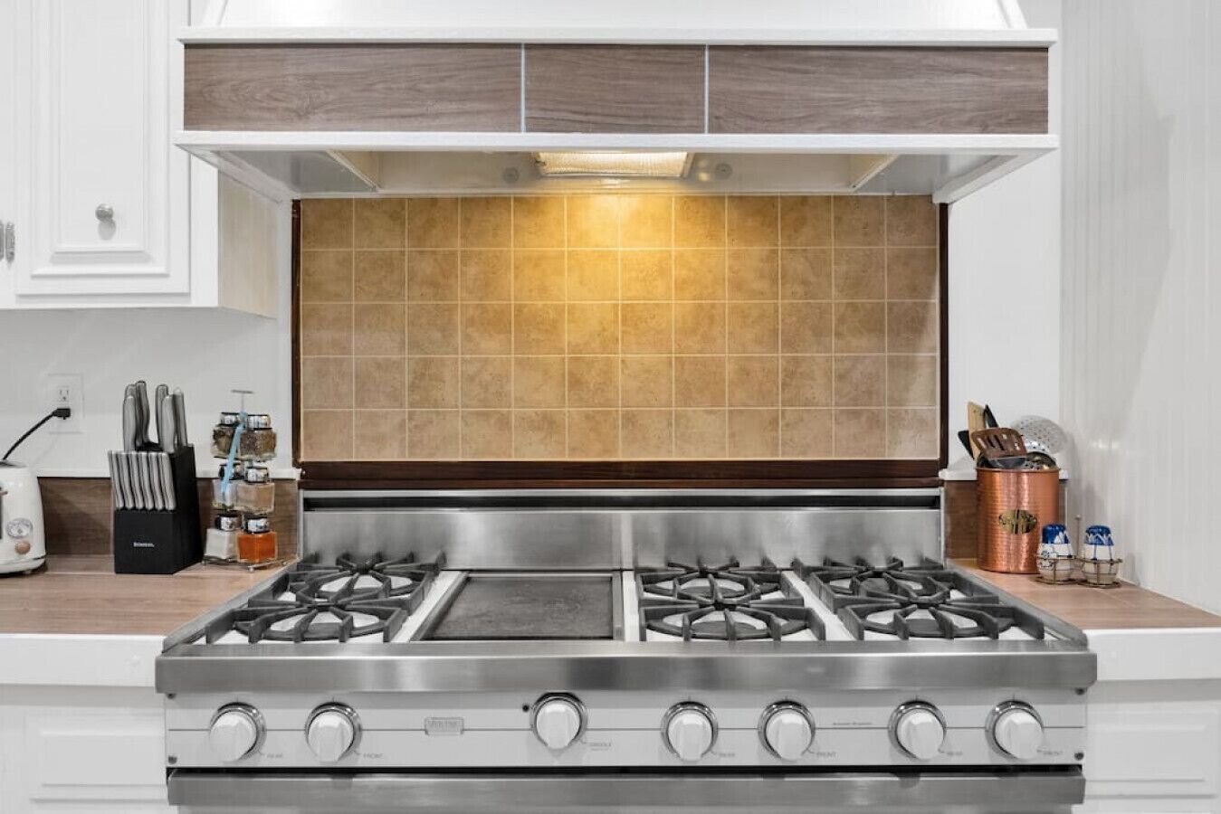 A kitchen with a stainless steel stove, white cabinets, and a backsplash with a wooden panel design.
