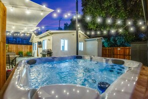 A hot tub in a backyard with a house, string lights, and a wooden fence. - Modern Cottage, Jacuzzi, Bistro Patio, Walk to Everything! (Thousand Oaks)