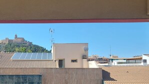 A view of a building with a tiled roof and solar panels, overlooking a hill with a castle-like structure.
