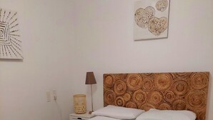 A neatly made bed with white linens, a wooden headboard, and a small bedside table with a lamp and a decorative item.