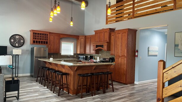 A kitchen with wooden cabinets, a stainless steel refrigerator, a bar area with stools, and pendant lighting. - Stay in Comfort at Corky's Cove Unit #1. (Port Mansfield)