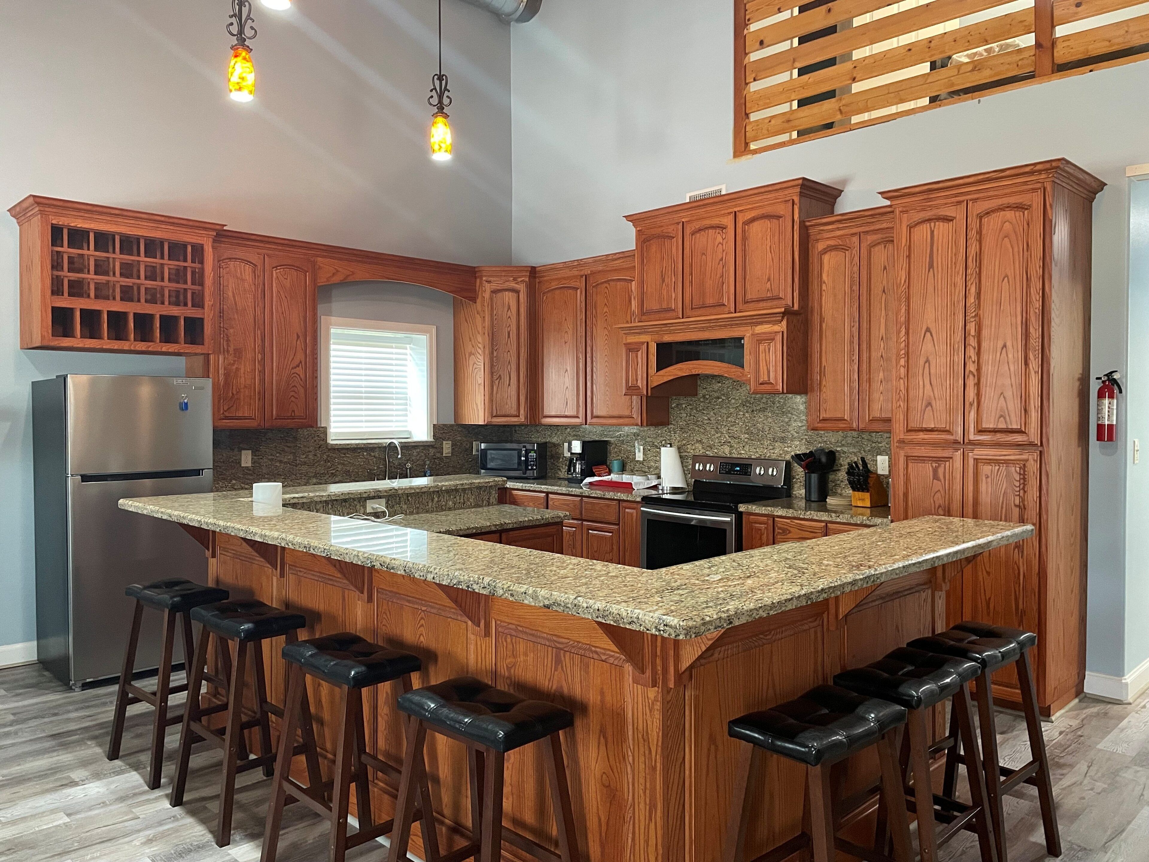 A kitchen with wooden cabinets, a granite countertop, stainless steel appliances, and bar stools.