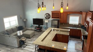 A modern kitchen with granite countertops, wooden cabinets, and a central island with bar stools. - Stay in Comfort at Corky's Cove Unit #1. (Port Mansfield)
