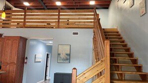 A wooden staircase leading to an upper level, a dark cabinet, and a painting on the wall. - Stay in Comfort at Corky's Cove Unit #1. (Port Mansfield)