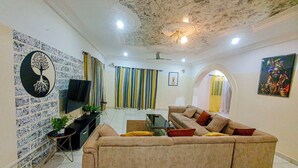 A living room with a sofa, TV, and curtains. - The Unique and Tranquil Retreat Apartment (Brufut)