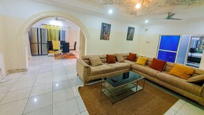 A living room with a sectional sofa, a glass coffee table, a ceiling fan, and a dining area in the background. - The Unique and Tranquil Retreat Apartment (Brufut)