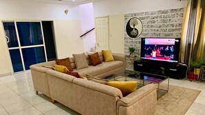 A living room with a beige sofa, a television, and a patterned wall. - The Unique and Tranquil Retreat Apartment (Brufut)