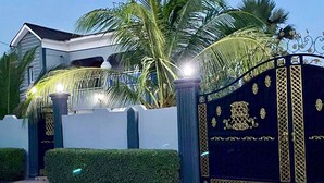 A gated entrance with a palm tree and a building in the background. - The Unique and Tranquil Retreat Apartment (Brufut)