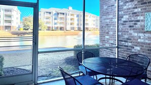 A room with a large window overlooking a building and a body of water. There is a round table with chairs and a brick wall. - Book your Spring Golf Vacations. Summer Beach vacations are here too.  (Myrtle Beach)
