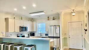 A modern kitchen with white cabinetry, stainless steel appliances, and a bar area with stools. - Book your Spring Golf Vacations. Summer Beach vacations are here too.  (Myrtle Beach)