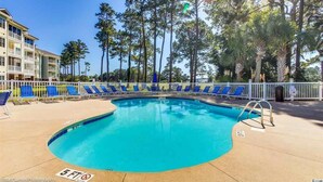 A swimming pool with blue chairs and a white fence, surrounded by tall trees. - Book your Spring Golf Vacations. Summer Beach vacations are here too.  (Myrtle Beach)