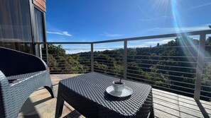 A balcony with a table and chair, a cup, and a scenic view of a forested area. - Arisa Mountain House (San Isidro)