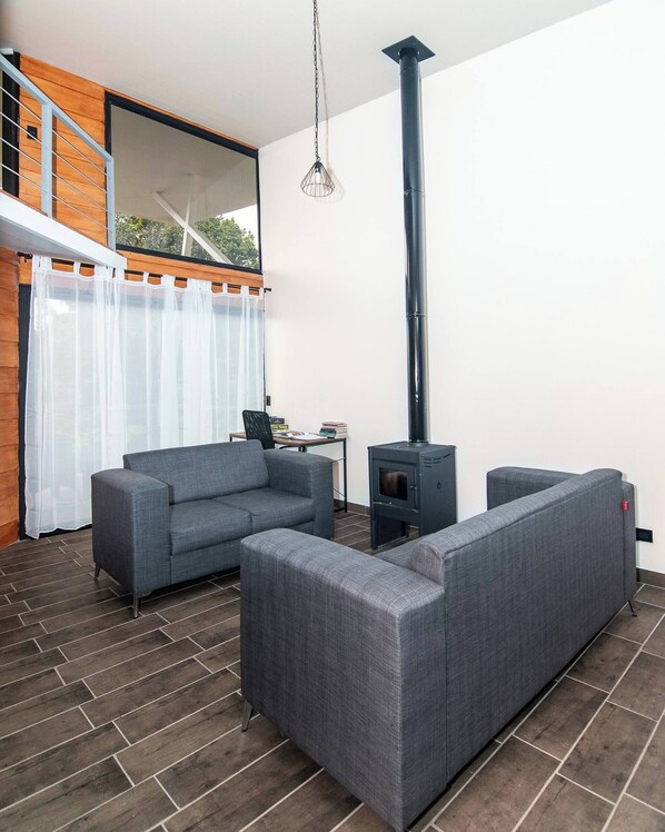 A modern living room with a sofa set, a fireplace, and a view of a wooden balcony. - Arisa Mountain House (San Isidro)