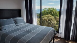 Ein Schlafzimmer mit einem großen Bett, dunklen Vorhängen und Blick auf Bäume und Berge.