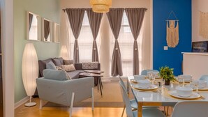 Ein modernes Wohnzimmer mit einer Couch, einem Esstisch für vier Personen und einer großen Stehlampe.