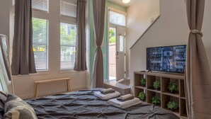 Ein Schlafzimmer mit einem Bett, einem Fernseher, einer Bank und einem Fenster mit Vorhängen.