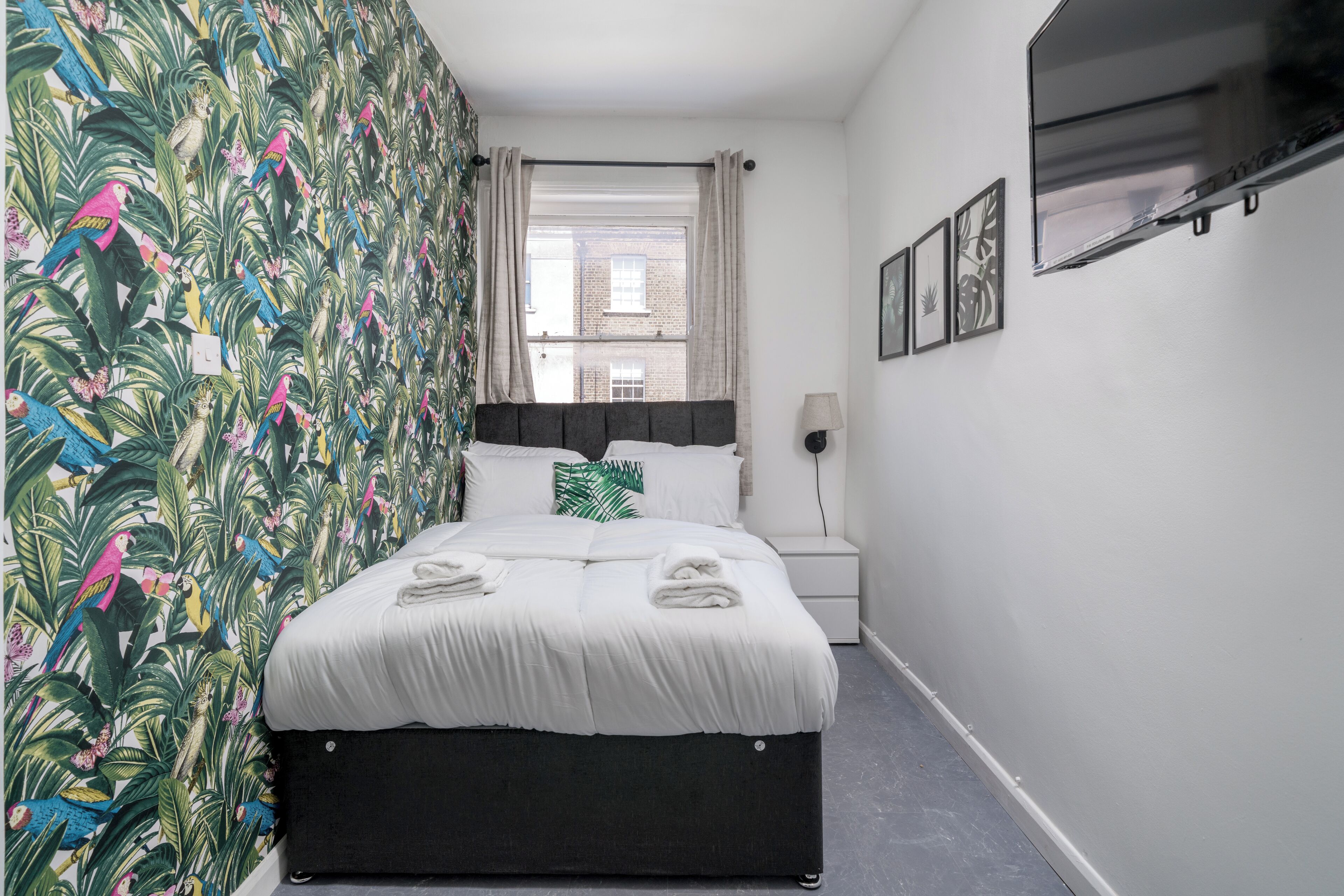A neatly made bed with white linens, a black headboard, and a window with curtains.