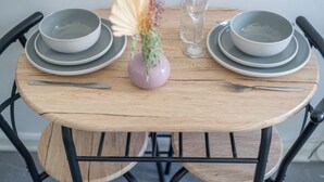 A round wooden table with grey plates and bowls, a pink vase with dried flowers, and a clear glass. - Studio Unit in Chapel Market London (London)
