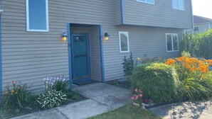 A two-story residential building with a blue front door, two windows on the first floor, and a small porch area with a light fixture. - Spacious beach house with front and back yards, short walk to Scarborough beach  (Narragansett)