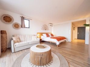A modern bedroom with a bed, a sofa, a round wooden table, and a woven rug. - Appartement Orient Bay-ti Paradise (Collectivité de Saint-Martin)