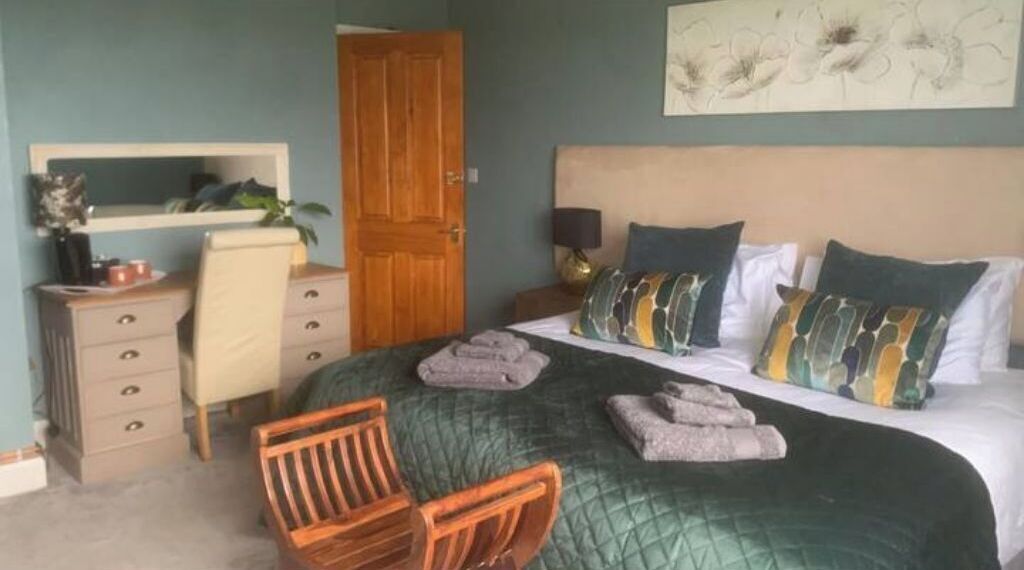 A bedroom with a bed, a chair, a dresser, a nightstand, and a door.