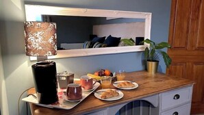 A breakfast setup with a coffee maker, mugs, croissants, and fruit on a wooden counter. - Mew Stone - A large double room with extensive views out to sea. (Millbrook)