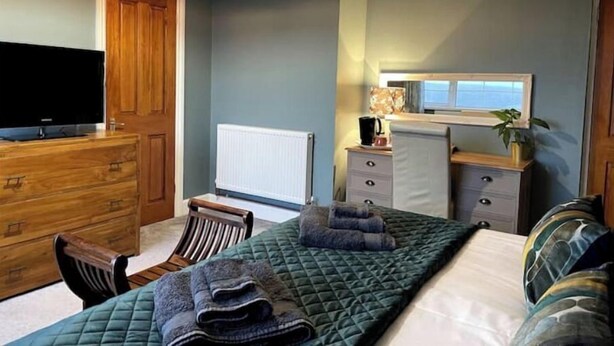 A bedroom with a bed, a dresser, a television, a radiator, and a window with a view. - Mew Stone - A large double room with extensive views out to sea. (Millbrook)