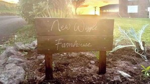 A wooden sign with the text "New Wiggle Farmhouse" in a rural setting with a sunset in the background. - Mew Stone - A large double room with extensive views out to sea. (Millbrook)