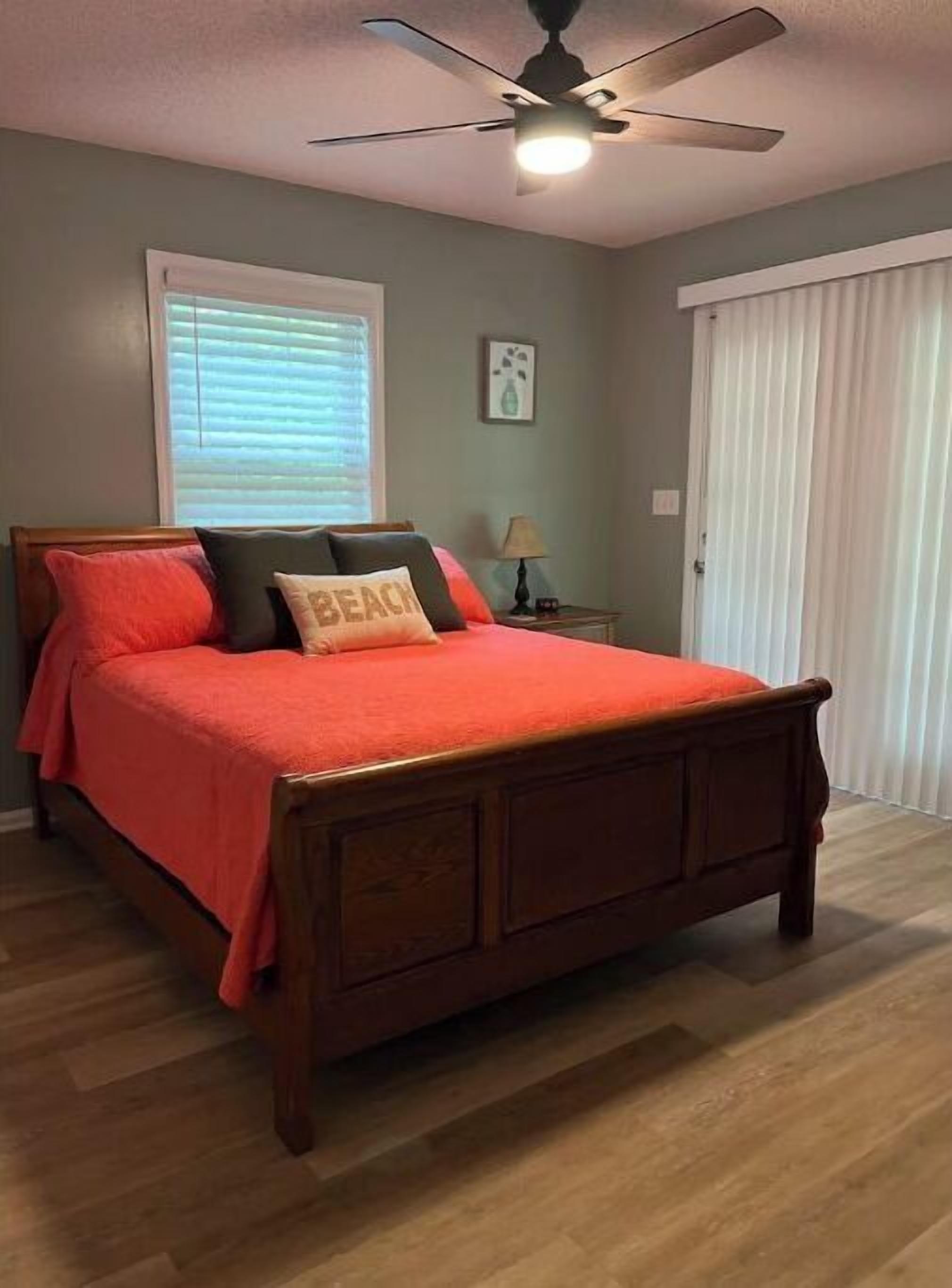 Une chambre à coucher avec un lit en bois, un ventilateur de plafond, une fenêtre avec des stores et une porte avec des rideaux.