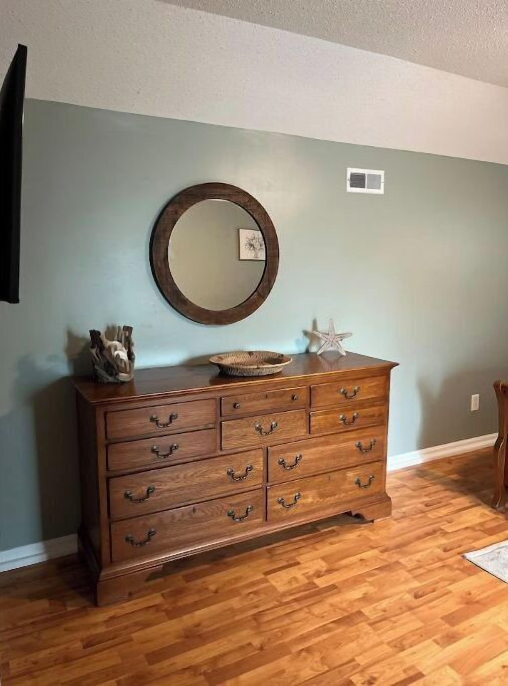A wooden dresser with six drawers, a round mirror, and decorative items on top.