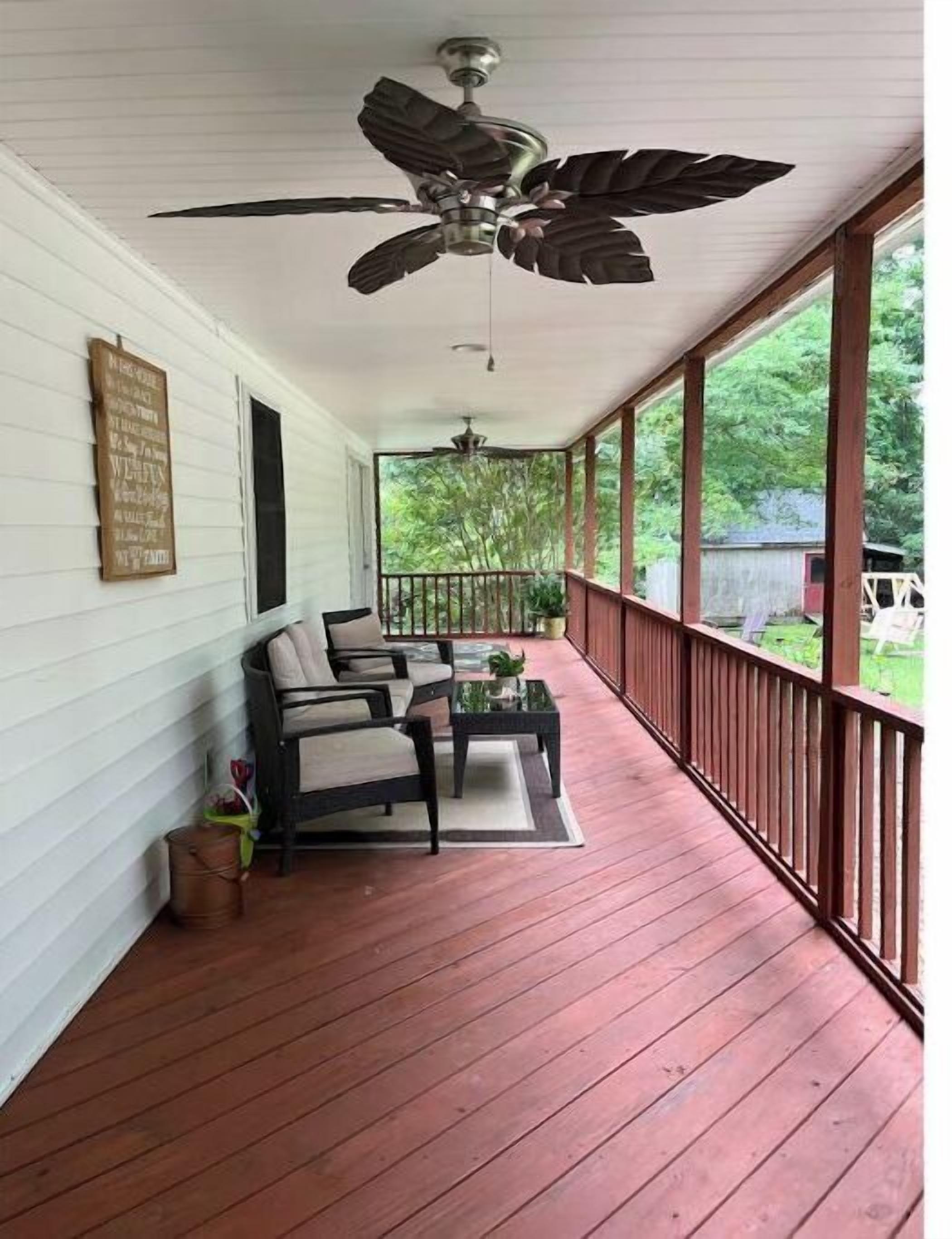 A covered porch with a ceiling fan, two chairs, a small table, and a wooden railing.