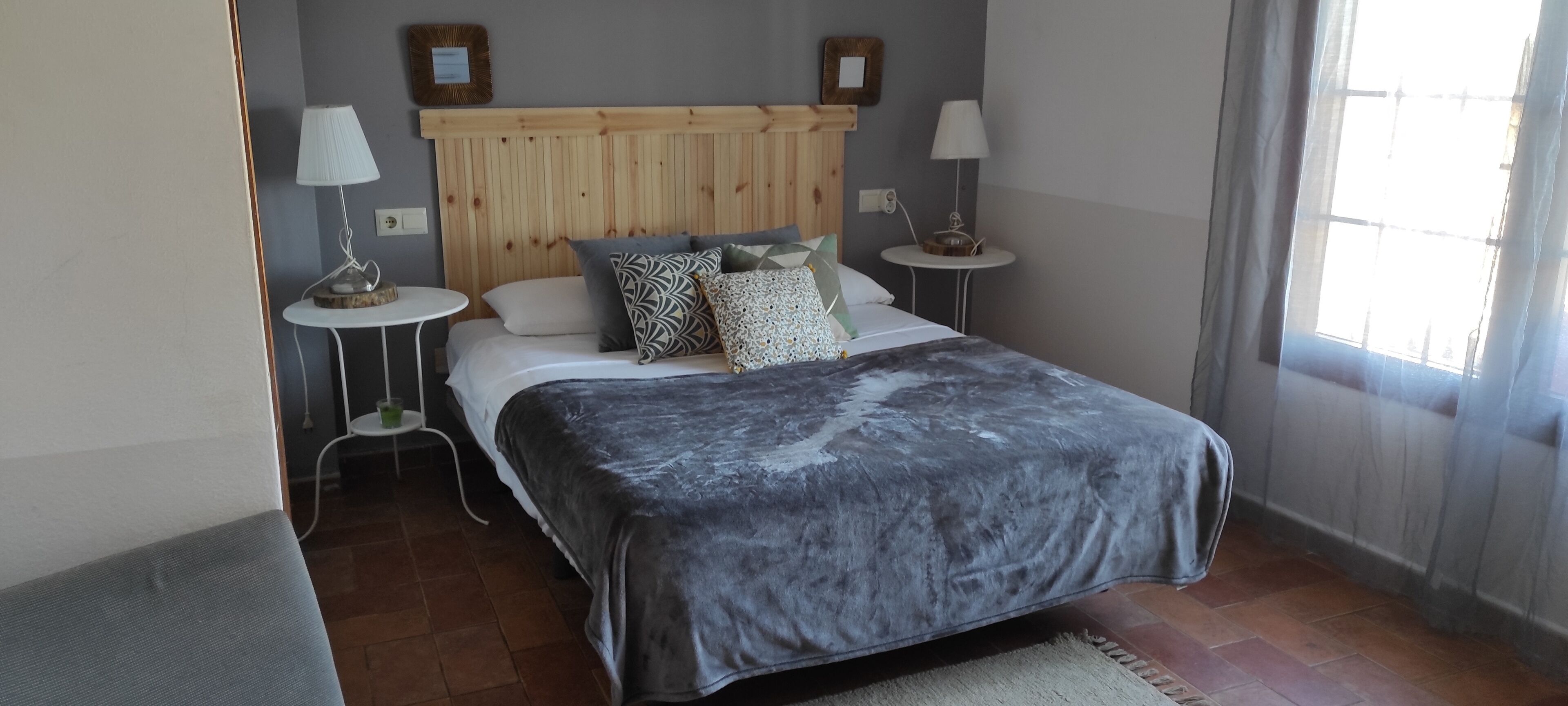 A bedroom with a wooden headboard, a bed with multiple pillows, two bedside tables with lamps, and a view of the outdoors through a window.