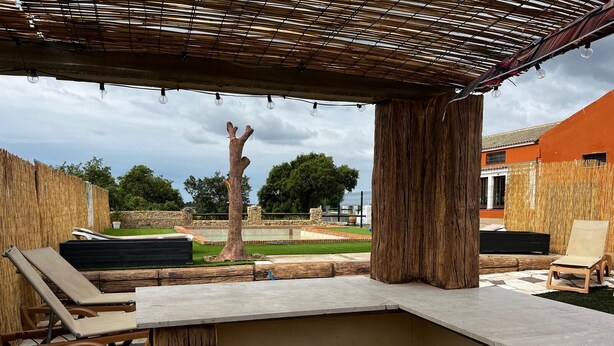 Ein Außenbereich mit Patio, einer Pergola, Liegestühlen und einer Steinmauer.