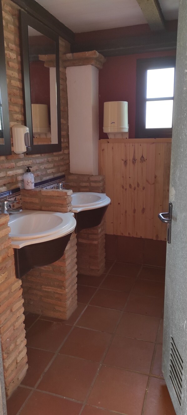 Une salle de bain avec deux lavabos, un miroir, un distributeur de savon liquide et une fenêtre.