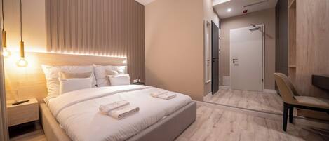 Una habitación de hotel moderna con una cama grande, mesitas de noche, una silla y una puerta que da a un baño.