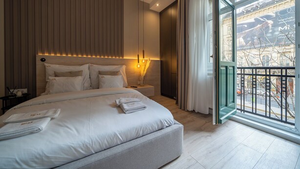 A modern hotel room with a large bed, bedside tables, and a view of the city through a large window. - Károly Boutique Suites, Best Location by BQA (Budapest)