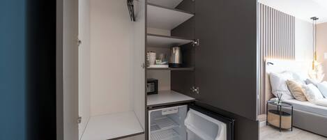 A compact kitchen with a refrigerator, a coffee maker, and a small shelf.