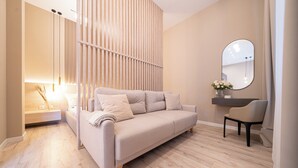 A modern, minimalist bedroom with a beige sofa, a bedside table, a mirror, and a wooden floor. - Károly Boutique Suites, Best Location by BQA (Budapest)