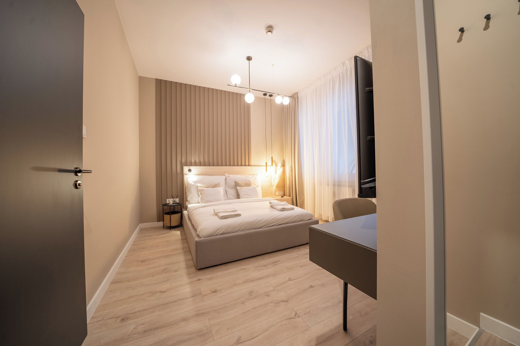 A modern hotel room with a large bed, bedside tables, a desk, and a flat-screen TV.
