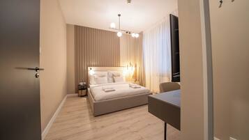 A modern hotel room with a large bed, bedside tables, a desk, and a flat-screen TV.