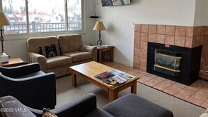 Una sala de estar con un sofá, una mesa de centro con revistas, una chimenea y un televisor montado en la pared.