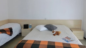 Camera d'albergo con due letti, un comodino con una lampada, una coperta e un peluche.
