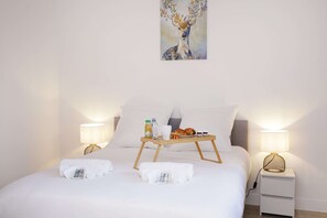 A neatly made bed with a tray of breakfast items, two bedside lamps, and a painting on the wall.