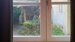Ein Fenster mit drei brennenden Kerzen auf einem Fensterbrett, mit Blick auf einen Garten mit Pflanzen und einem Gebäude im Hintergrund.