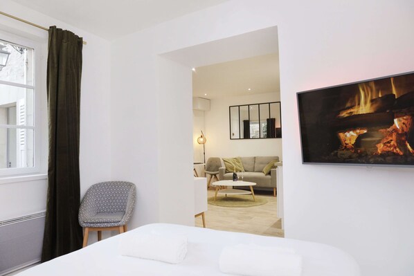 A hotel room with a bed, a chair, a sofa, a TV, and a fireplace.