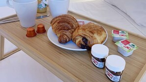Ein Frühstücksbrett mit Croissants, Nutella und Joghurt auf einem Bett.