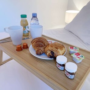 A breakfast tray with croissants, Nutella, and yogurt on a bed.