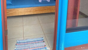 A room with two beds, a wooden floor, a door, and a window with curtains. - Sunrise  (Drake Bay)