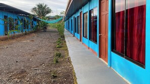 A building with blue exterior walls, large windows with red curtains, and a concrete pathway. - Sunrise  (Drake Bay)