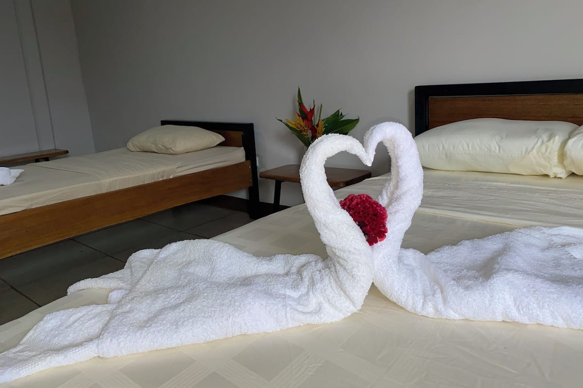 A hotel room with two beds, one with a heart-shaped towel decoration and a red flower.